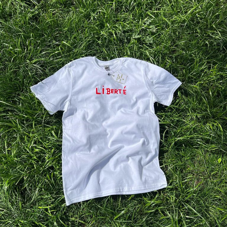 თეთრი-მაისური-წარწერით-liberte Stagi Group, სტაგი ჯგუფის თეთრი მაისური, წითელი წარწერა, LIBERTE, ხავერდის დიზაინი, ბალახის ფონზე