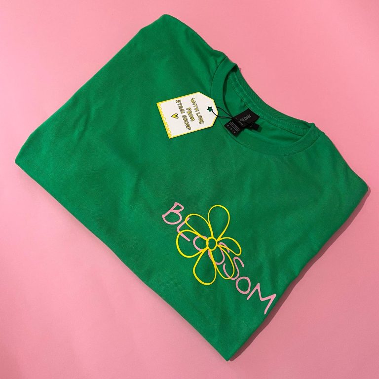 მწვანე-მაისური-წარწერით-blossom Stagi Group, სტაგი ჯგუფის მწვანე მაისური, ვარდისფერი წარწერა, BLOSSOM, ყვავილის ყვითელი დიზაინით, ვარდისფერ ფონზე